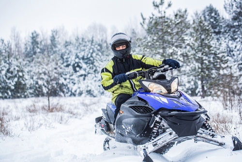 Man driving snowmobile in snowy forest. 