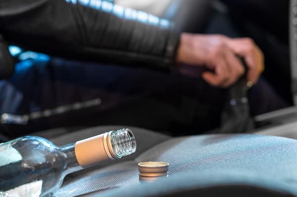 Drunk driver shifting gears with an empty wine bottle in the seat next to him