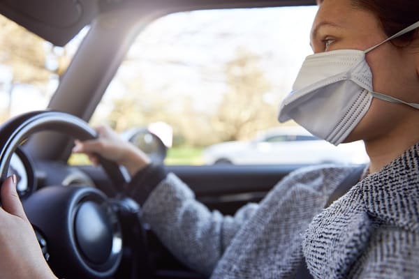 A woman wears a protective face mask while driving a car.