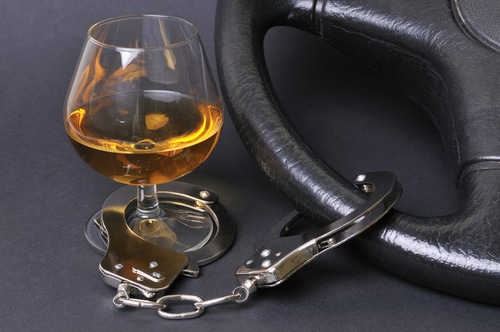 Image of glass of whiskey with handcuff connected to a car steering wheel.