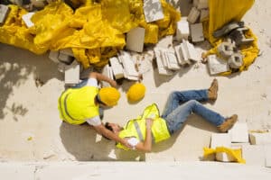 Top down image of an injured construction worker laying on the ground with a coworker kneeling to check on him
