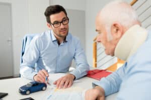 Older man wearing a neck brace and consulting with a personal injury lawyer after experiencing delayed injury