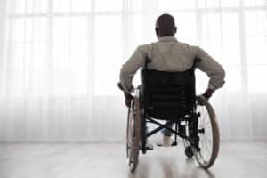 Man sitting in a wheelchair and facing toward a window after suffering mobility loss following an accident.