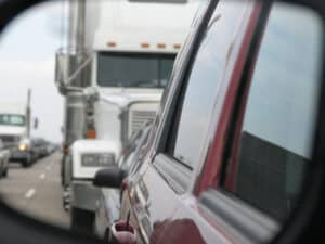 Large semi-truck seen tailgating in a rearview mirror, maybe leading to a negligent motor vehicle accident.