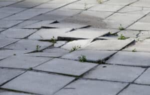 Cracked and uneven concrete at an apartment complex, posing a hazard that could cause personal injuries.